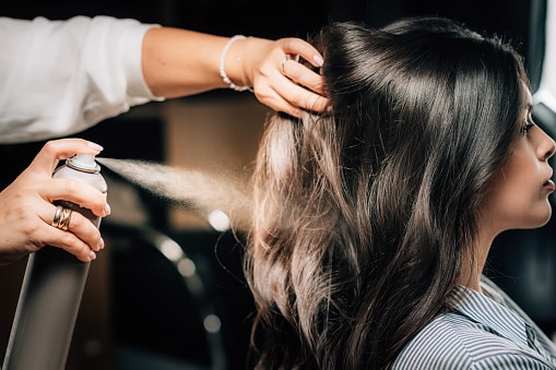 Hairdresser spraying woman’s long black hair with hair spray.